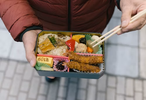 pria memegang kotak bekal bento dengan sumpit