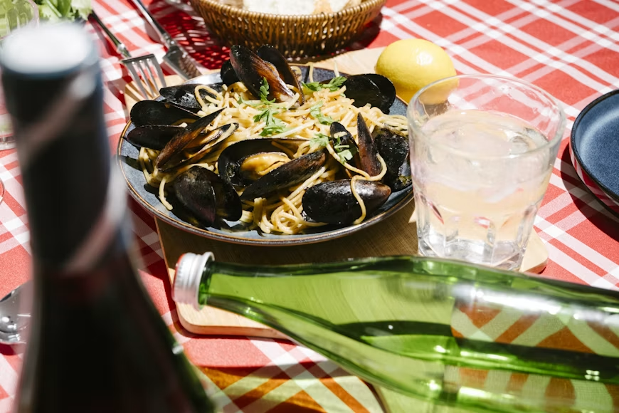 pasta italia dengan topping kerang dan minuman pada meja makan beralaskan kain merah bermotif kotak-kotak